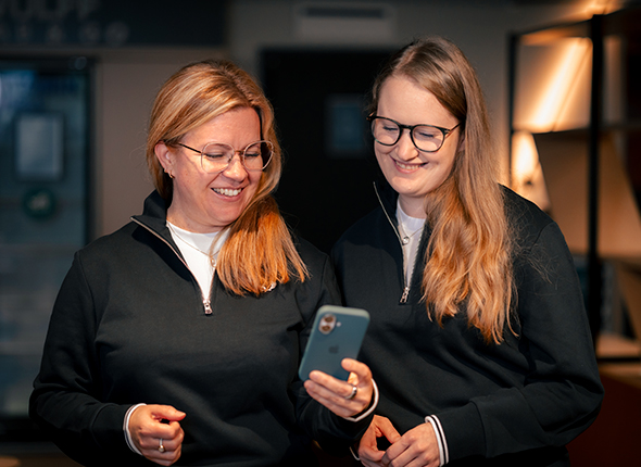 Kaksi-Wulff-Doctorsin-tyontekijaa-hymyilee-ja-tarkastelee-yhdessa-alypuhelinta-modernissa-toimistoymparistossa